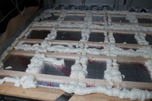 Expanding foam sealing insulation boards in a van conversion floor.